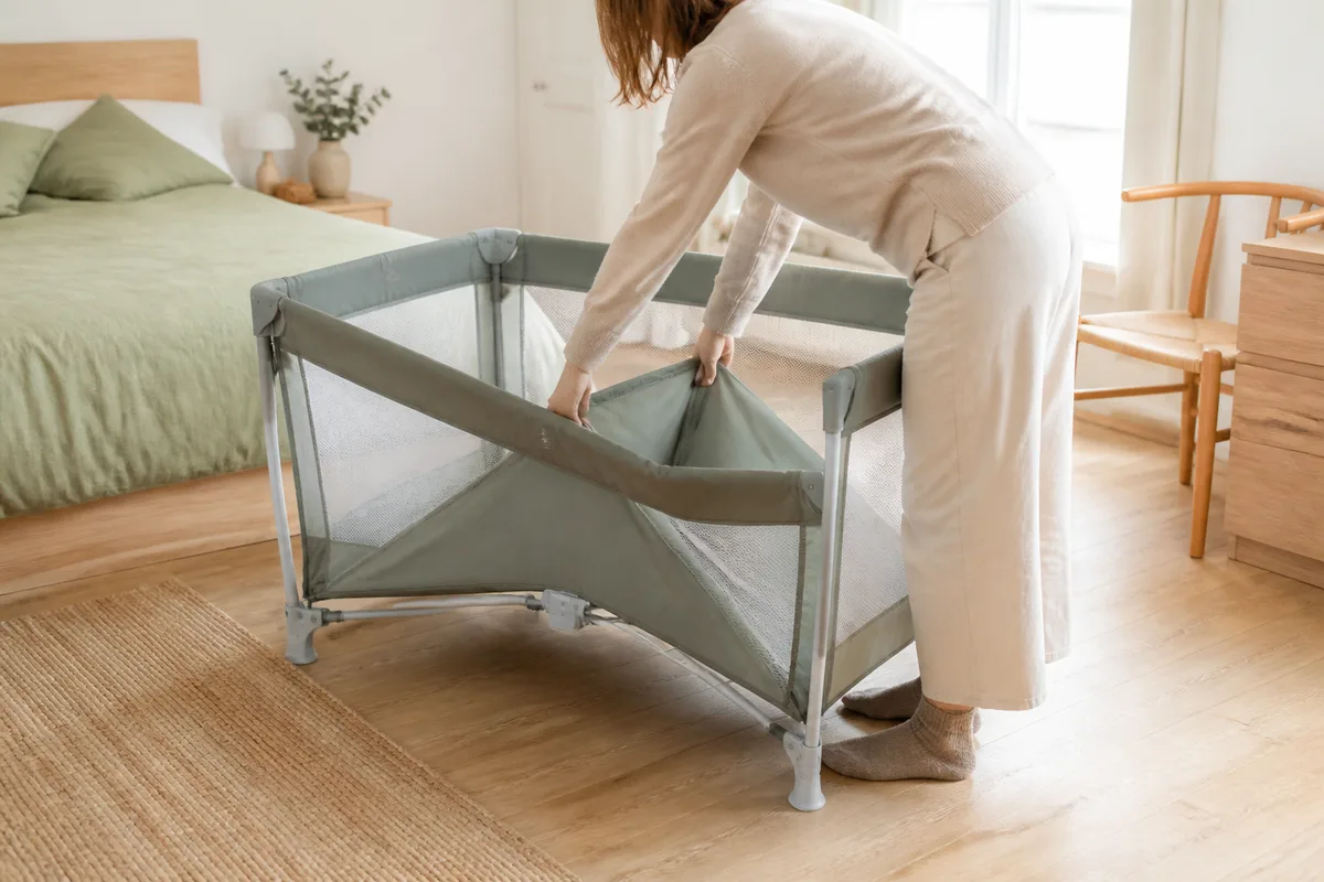 Adulte repliant un lit parapluie en soulevant le centre du fond dans une chambre claire
